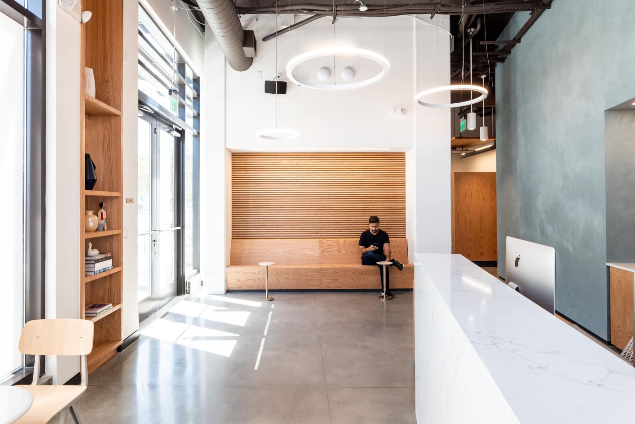 The bright lobby wrapped in fluted wood, with a guest at ease