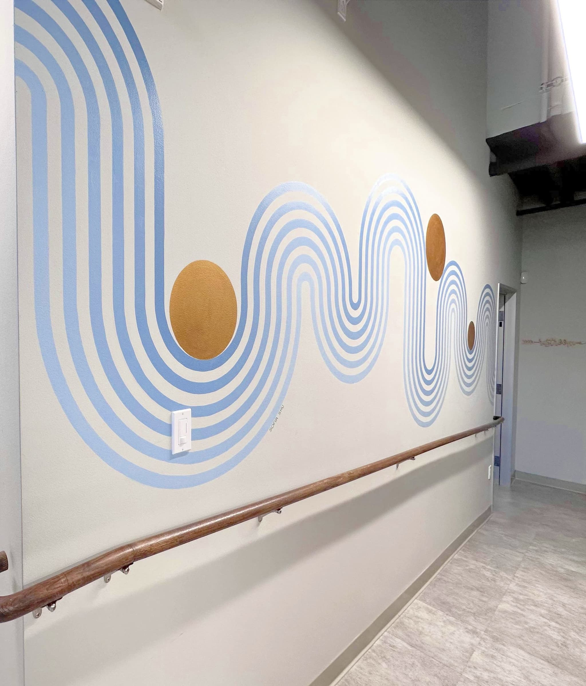 The hand painted blue wave mural with gold suns along the corridor wall at Zen Dental Studio San Francisco