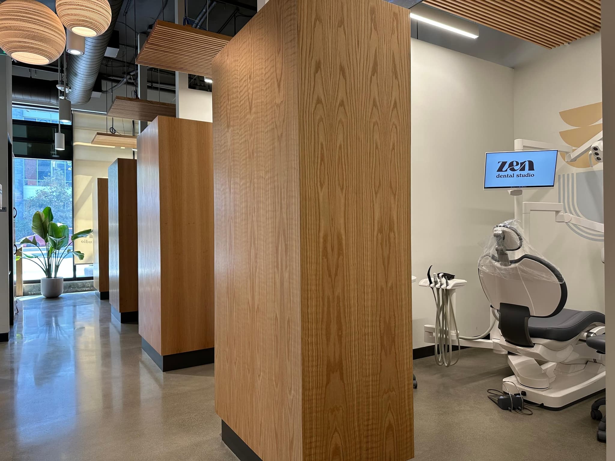 An open treatment bay at the Mountain View studio, with white oak partitions, an oak slat ceiling, and a screen at the chairside