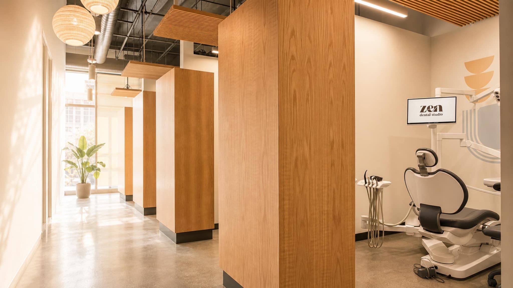 The corridor at the Mountain View studio, with white oak columns, woven pendant lanterns, and a treatment room open at the end